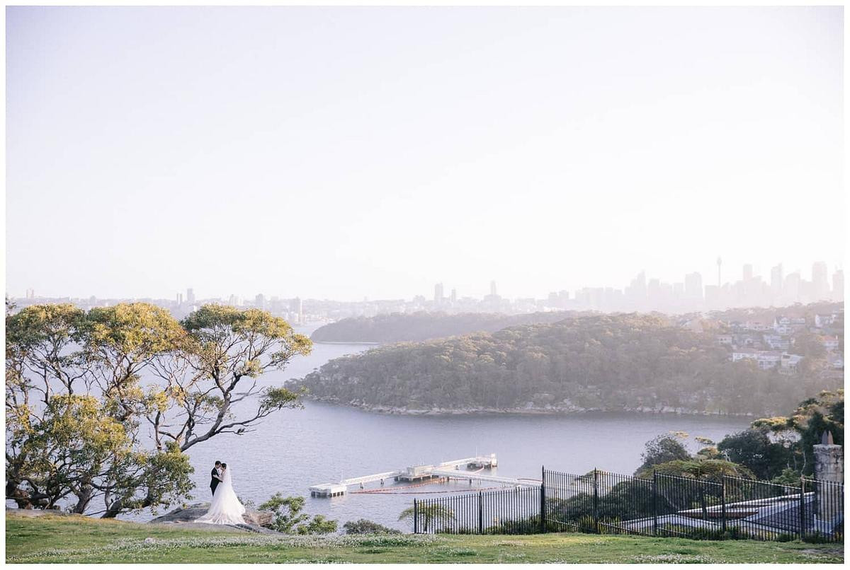 Scenic wedding photo of the newlyweds standing under at tree with a breathtaking backdrop at Georges Head Lookout Gunners Barracks Mosman.